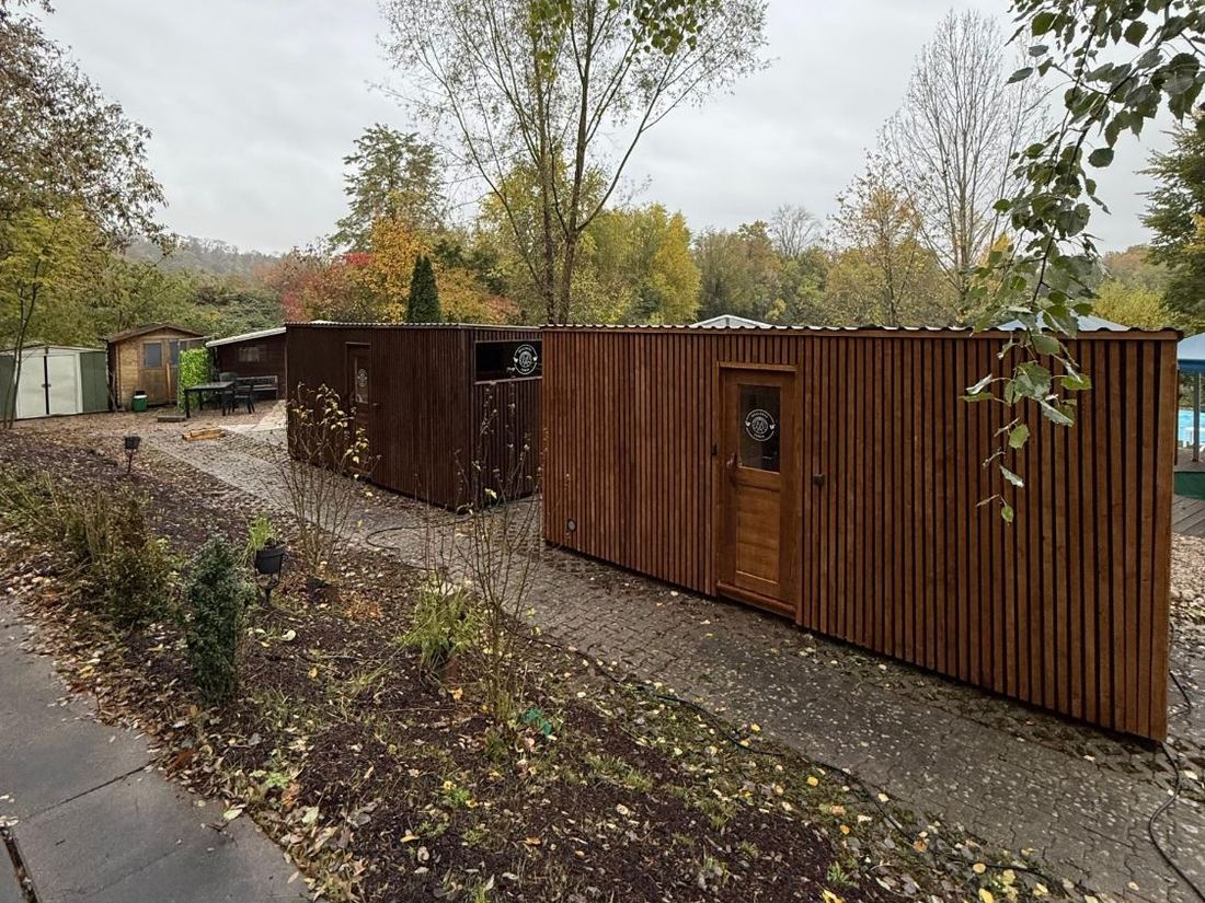Zwei Cubes mit Holzschalung in einem Garten im Herbst, auf gepflastertem Grund neben Beeten.